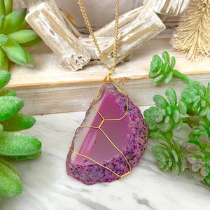 May include: A gold chain necklace with a pink and white agate pendant wrapped in gold wire.