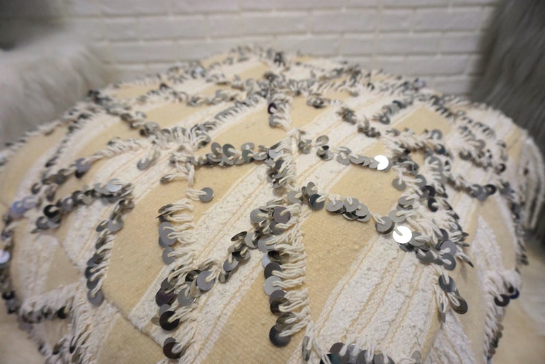 May include: A cream-colored throw pillow with white fringe and silver sequins. The pillow has a geometric pattern.