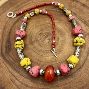 May include: A colorful necklace featuring a mix of yellow, pink, and red beads. The necklace has silver-toned metal accents and a toggle clasp. The beads are irregularly shaped, giving the necklace a unique, handcrafted look.