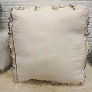 May include: A white square pillow with a fringe border. The pillow is made of a soft, textured fabric and has a subtle sheen.