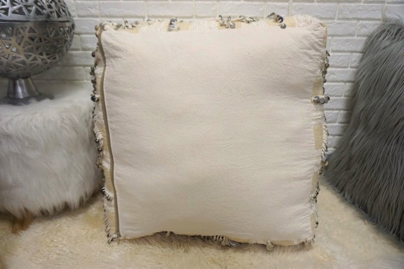 May include: A white square pillow with a fringe border. The pillow is made of a soft, textured fabric and has a subtle sheen.