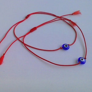 May include: Two red string bracelets with blue evil eye charms. The charms have a white centre.