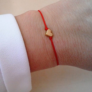 May include: A red string bracelet with a small gold heart charm.