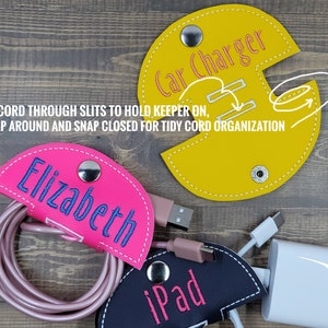 May include: Three cord organizers made of fabric with snap closures. The organizers are yellow, pink, and black. The yellow organizer has the text "Car Charger" embroidered on it. The pink organizer has the text "Elizabeth" embroidered on it. The black organizer has the text "iPad" embroidered on it.