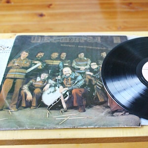 May include: A vintage vinyl record album cover featuring a band called "MEGARA" with a group of musicians in colorful clothing. The album cover is brown and has a black vinyl record on top of it.