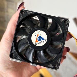 May include: A black computer fan with a central logo that reads "GlacialTech". The fan has black blades and a silver heat sink. The fan is square and has mounting holes in each corner.