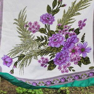 May include: A white fabric square with a green border and a floral pattern. The pattern features purple and pink flowers with green leaves.
