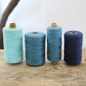 May include: Four spools of thread in shades of blue, from light to dark. The spools are made of wood and have a cardboard center.
