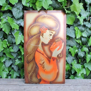 May include: A vintage wall art piece featuring a woman with long brown hair holding a red flower. The woman is wearing a long orange dress with gold accents. The background is a gold and brown color.