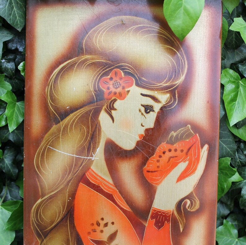 May include: A vintage painting on wood panel depicting a woman with long brown hair wearing a red dress and holding a red and white animal in her hands. The woman has a flower in her hair and is looking down at the animal.
