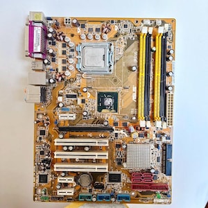 May include: A computer motherboard with various components, including a CPU, RAM slots, and expansion slots. The board is primarily gold with accents of purple, yellow, black, and red. It is a complex electronic circuit board.