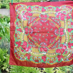 以下が含まれることがあります： 赤い花柄の正方形の布。柄は赤、緑、黄、青の花で構成されています。布はフリンジの縁取りがされています。