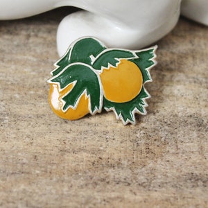 May include: A silver pin with a green and yellow enamel design of a hazelnut.