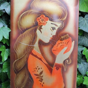 May include: A vintage painting on a wooden panel depicting a woman with long brown hair wearing a red and orange dress. She is holding a small orange object in her hand and looking down at it.