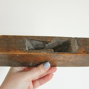 Op de afbeelding: Een vintage houten handvlak met een verweerde bruine afwerking. Het vlak is rechthoekig van vorm met een licht gebogen bovenkant en een handvat aan de linkerkant.