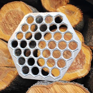 May include: A silver metal hexagonal mold with 36 round holes for making dumplings or other small food items.