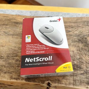 May include: A boxed Genius NetScroll mouse, featuring a white and gray design. The packaging is red and white, with the Genius logo and product details. The box includes text about the mouse's features and compatibility with Windows XP/Me/2000/98.