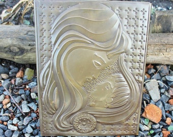 May include: A metal wall plaque with a raised relief design of a mother and child. The mother's hair is flowing and she is looking down at the child. The child is looking up at the mother. The plaque is a light gold color and has a textured background.