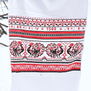 Puede incluir: Tela blanca con diseños bordados en rojo y negro. El texto "КИЕВУ 1500 ЛЕТ" está bordado en negro.