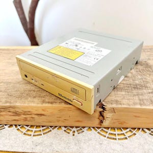 May include: A beige and gray computer CD-ROM drive. The drive has a yellow front panel with a disc symbol and the text "52x32x52x". The top of the drive has a yellow sticker.