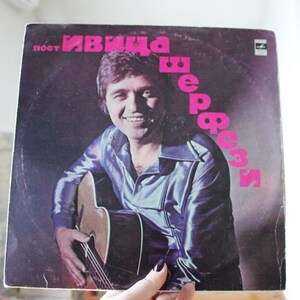 May include: A vintage vinyl record album cover featuring a man with a guitar. The album title is "Иван  Вербич" in pink lettering. The album cover is a dark brown color with a purple hue.