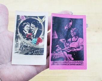 Puede incluir: Dos postales vintage. Una presenta una imagen en blanco y negro de una pareja en un marco circular, con un tren y texto en ruso. La otra es rosa con una pareja y texto en ruso. Las postales se sostienen en una mano.