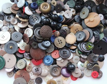 May include: A collection of various buttons in different sizes, shapes, and colors. The buttons are made of materials like plastic, wood, and metal. Colors include black, white, brown, red, green, and blue. Some buttons have two or four holes, while others have shanks.