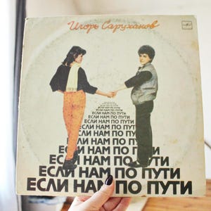 May include: A vintage vinyl record album cover featuring a black and white photo of two people holding hands. The album is titled "Igor Sarukhanov" and the text "ESLI NAM PO PUTI" is repeated multiple times in a pyramid shape.