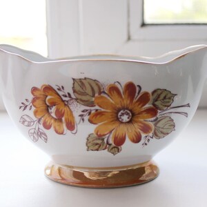 May include: A white ceramic gravy boat with a gold rim and floral design featuring brown and orange flowers.