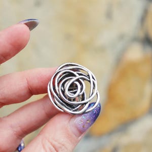 Puede incluir: Pinza para el pelo de metal plateado en forma de rosa. La pinza está hecha de múltiples bucles entrelazados.