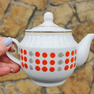 May include: White teapot with a gold trim and red polka dots. The teapot has a lid and a handle.