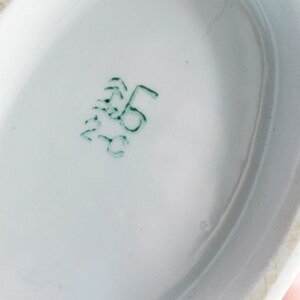 May include: Close-up of the underside of a white porcelain dish with a green mark that reads "5" in a circle.