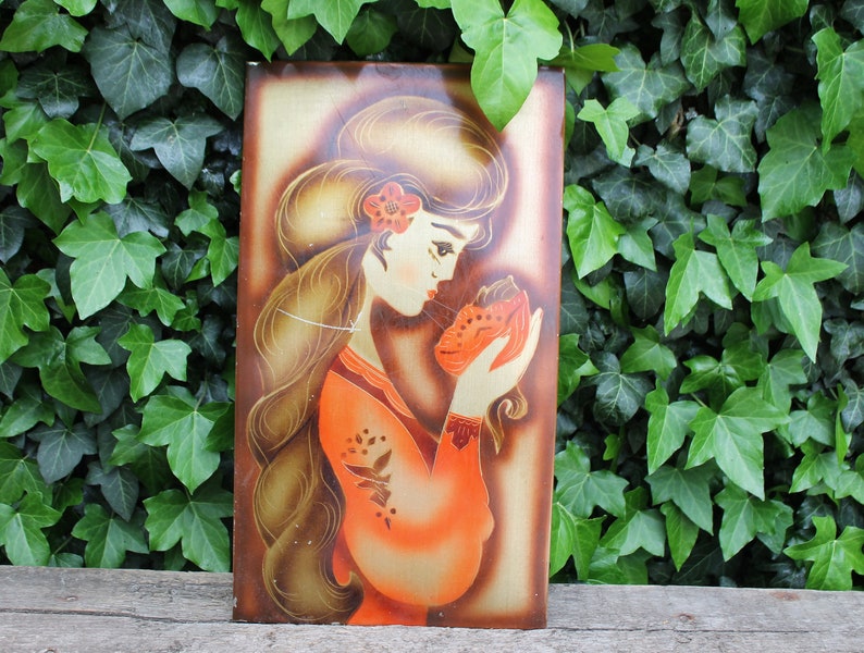 May include: A vintage wall art piece featuring a woman with long brown hair wearing a red dress and holding a small orange animal. The background is a gold metallic color.