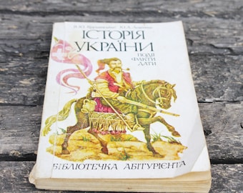 May include: A vintage book cover with a yellowed background and a colorful illustration of a man on horseback. The title of the book is "Історія України" which translates to "History of Ukraine". The book is part of a series called "Бібліотечка абітурієнта" which translates to "Library for Applicants".