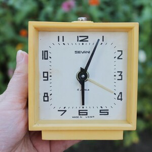 Peut inclure: Un réveil vintage jaune avec des aiguilles et des chiffres noirs. Le cadran de l'horloge indique "SEVANI 4 JEWELS MADE IN USSR".