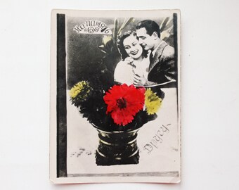 Puede incluir: Una postal vintage con una foto en blanco y negro de una pareja abrazándose. La foto está rodeada de un ramo de flores rojas, amarillas y blancas en un jarrón negro. El texto "Ha Nama" y "Dpeyey" está escrito en la postal.