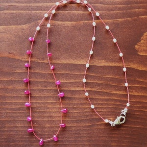May include: A delicate necklace with pink and white beads on a thin red string. The necklace has a silver clasp.