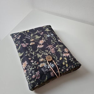 May include: A rectangular, dark navy blue fabric case with a floral pattern. The pattern includes pink, yellow, and blue flowers with green leaves and stems. A wooden button and pink elastic secure the case.