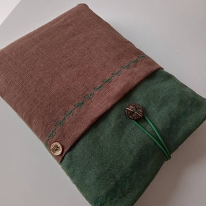 May include: A two-toned, handmade fabric case. The top flap is brown with green stitching and a wooden button closure. The bottom section is green, secured with a green elastic cord and a wooden button.