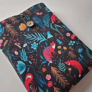 May include: A black fabric pouch with a drawstring closure and a wooden button. The pouch features a repeating pattern of red foxes, blue and green leaves, and colorful flowers on a black background.