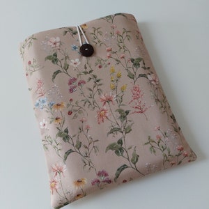 May include: A beige fabric laptop sleeve with a floral pattern featuring pink, yellow, and blue flowers. The sleeve has a brown button closure and a white elastic strap.