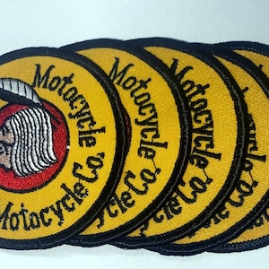 Könnte beinhalten: Ein Stapel runder, gelber Aufnäher mit schwarzem Rand. Jeder Aufnäher zeigt die schwarzen Worte "Indian Motorcycle Co." um einen roten Kreis mit einem Profil eines indianischen Kopfes. Die Aufnäher sind wahrscheinlich für Kleidung oder Accessoires.