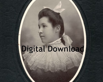 May include: A black and white portrait of a young woman with a white bow in her hair. She is wearing a white lace collar and a dark dress. The portrait is framed in an oval.