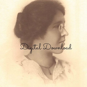 May include: A sepia-toned portrait of a woman wearing round glasses and a lace collar. Her hair is styled in a bun and she is looking to the side.