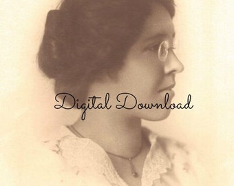 May include: A sepia-toned portrait of a woman wearing round glasses and a lace collar. Her hair is styled in a bun and she is looking to the side.