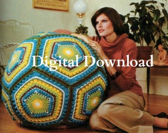 Puede incluir: Un gran cojín de suelo de crochet de forma geométrica multicolor. El cojín está hecho de hilo azul, verde, amarillo y blanco. El cojín está sentado en un suelo de madera. Una mujer está sentada en un sofá detrás del cojín.