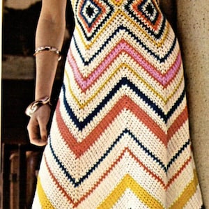May include: A woman wearing a crochet dress with a chevron pattern in white, pink, yellow, blue, and red. The dress has a sleeveless design and a scoop neckline.