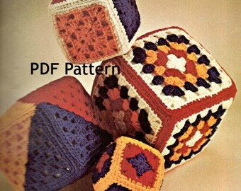 May include: A set of four crocheted cubes in various colours, including red, orange, yellow, white, and blue. The cubes are made with a granny square pattern and have a textured surface. The cubes are arranged in a pile, with the largest cube on top. The image includes the text "PDF Pattern".