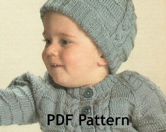 Puede incluir: Un cárdigan de punto gris para bebé con un patrón de trenza y botones. El cárdigan lo lleva puesto un bebé que lleva un gorro de punto gris a juego con un pompón en la parte superior. El texto "PDF Pattern" está impreso en la parte delantera del cárdigan.