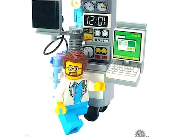 May include: A LEGO® hospital set with a doctor minifigure, a medical equipment cart with a digital clock, a computer monitor, and a keyboard. The cart has a gray base with a white top and a black keyboard. The doctor minifigure is wearing a white lab coat, a blue shirt, and a stethoscope. The set is designed by Brickis.